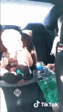 a baby in a car seat next to a bottle of soda and a tiktok logo