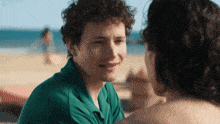 a young man in a green shirt looks at a woman on the beach