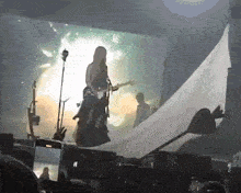 a woman is playing a guitar on a stage while a man stands behind her .