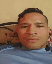 a man in a blue shirt is laying on a bed and making a funny face