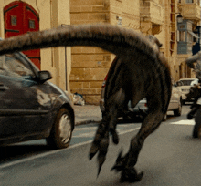 a dinosaur is walking down a street with a car behind it