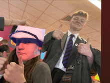 a boy in a suit and tie giving a thumbs up next to a girl with a mask on her face