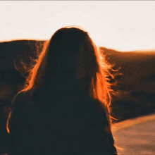 a woman with long hair is standing on a hill looking at the sunset