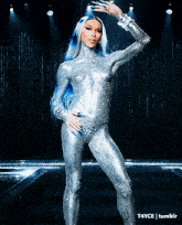 a woman with blue hair is standing in a silver bodysuit on a stage