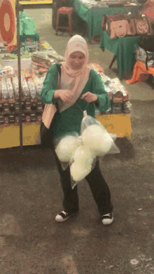 a woman in a hijab is holding a bag of cotton candy in front of a sign that says ' 0 '