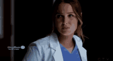 a woman in a white coat and blue scrub is crying in a dark room .