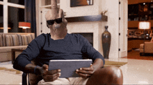 a man wearing sunglasses is sitting in a chair holding a tablet