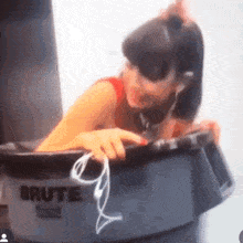 a woman is sitting in a brute trash can with headphones .