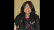 a man with long hair is sitting in front of a sign that says itua