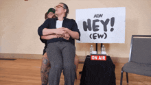 two people hugging in front of a sign that says hey ew