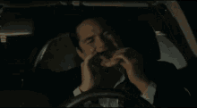 a man in a suit and tie is driving a car and eating a sandwich