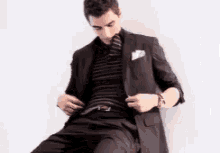 a man in a suit is adjusting his belt while sitting down