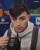 a man wearing a grey sweatshirt is holding a black microphone that says barça one