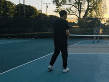 a man in a black shirt stands on a tennis court watching another man play tennis