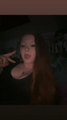 a woman with long red hair is making a peace sign with her tongue out in a dark room .