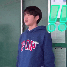 a young man wearing a blue hoodie with the word pop on it is standing in front of a green board .