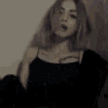 a woman with purple hair is wearing a black top and standing in a room .