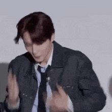 a man in a denim jacket and tie is dancing in front of a white wall .
