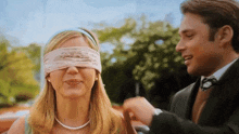 a woman with a blindfold on her eyes looks at a man