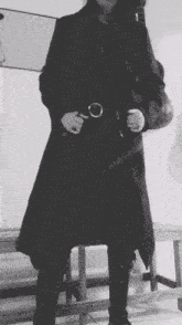 a black and white photo of a person in a long black coat