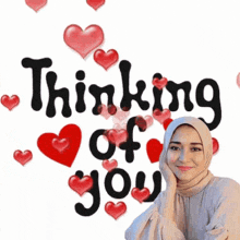 a woman in a hijab is standing in front of a sign that says `` thinking of you '' with hearts around her .