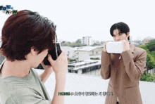 a man taking a picture of another man with the word now on the bottom right
