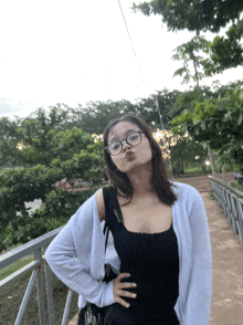 a girl wearing glasses and a black tank top stands in front of a railing