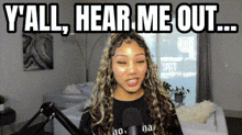a woman is standing in front of a microphone in a living room with the words `` y all , hear me out ... ''