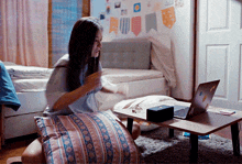 a girl is sitting on a pillow in front of a laptop
