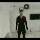 a man in a black jumpsuit is standing in a living room with a donut on the wall .