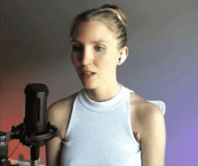 a woman in a white tank top singing into a black microphone