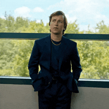 a man in a blue suit is leaning against a window