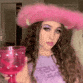 a woman in a pink cowboy hat is holding a pink glass .