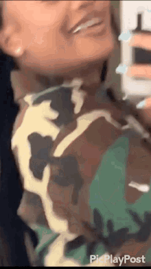 a woman in a camouflage shirt is smiling and taking a selfie .