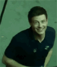 a man in a blue shirt is waving his hand and smiling