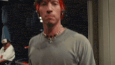 a man with red hair is wearing a gray shirt and a necklace .
