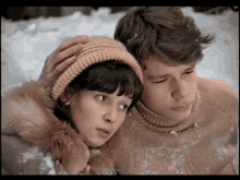 a boy and a girl are standing in the snow looking at something