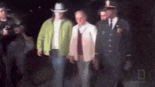 a group of men standing next to each other in a dark room . one of the men is wearing a cowboy hat .
