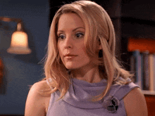 a blonde woman wearing a purple top with a brooch that says ' swirl ' on it