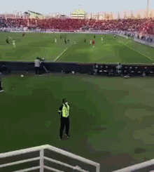 a man in a yellow vest stands on a soccer field watching a game