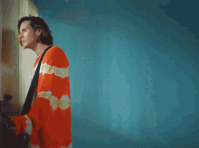 a man in an orange and yellow striped sweater is standing in front of a blue wall