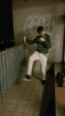 a young man standing on a balcony wearing a green hoodie that says ' sydney oxford ' on it