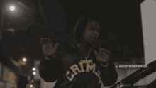 a man in a hoodie is standing next to a car at night and holding a gun .