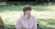 a young man in a pink hoodie is sitting on a blanket in a field