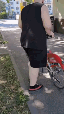 a man in a black tank top and shorts is standing next to a bicycle .