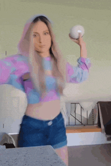 a woman in a blue and purple crop top is holding a blue ball