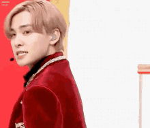 a young man in a red jacket is standing in front of a yellow wall .