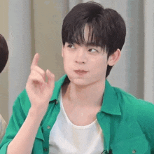 a young man in a green shirt is making a funny face and pointing up .