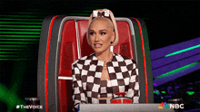 a woman in a checkered jacket is sitting in a chair with nbc written on the bottom