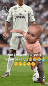 a soccer player wearing a fly emirates shirt is standing next to a baby
